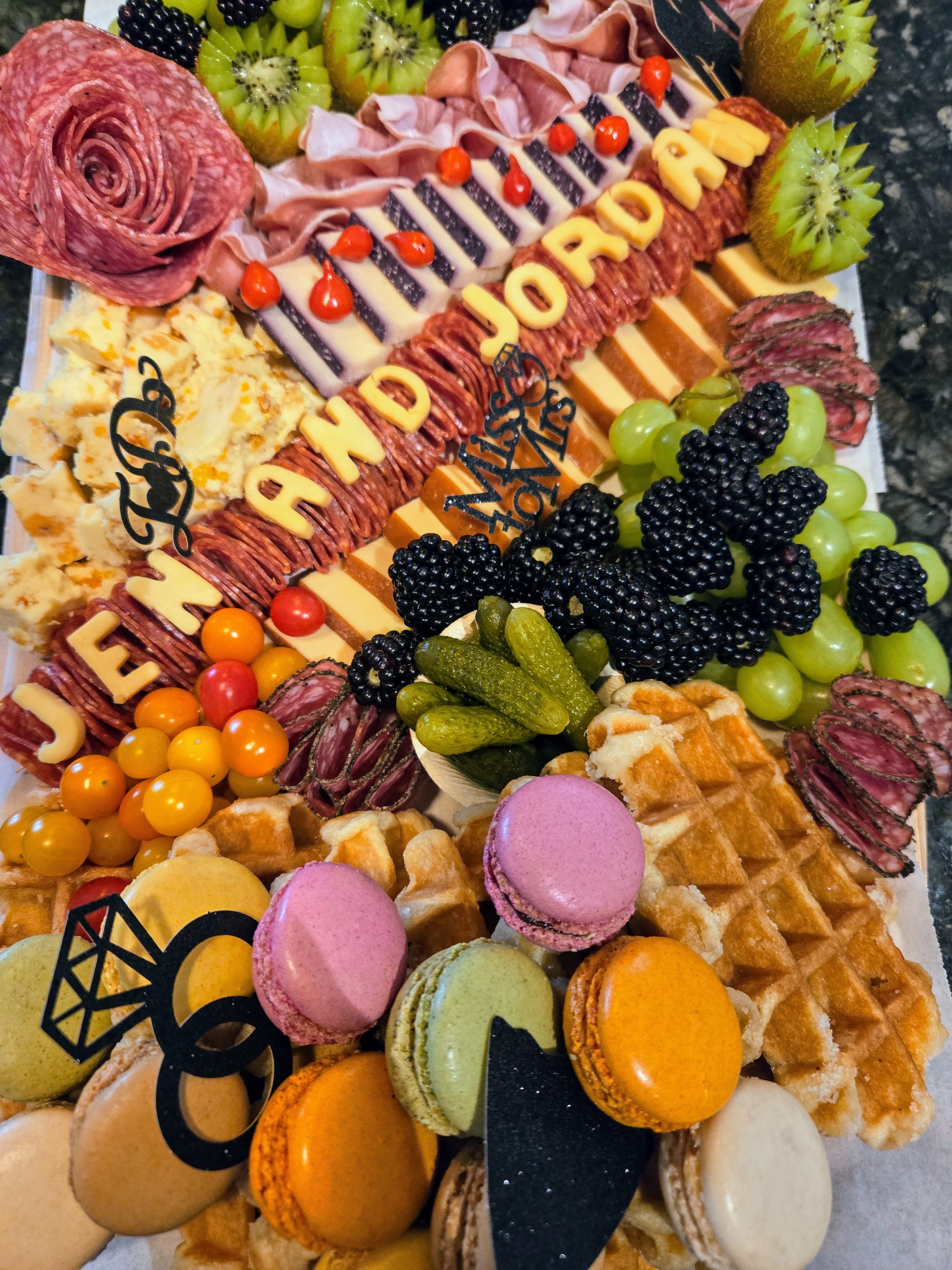 Custom wedding charcuterie grazing board with macarons, meats, fruits, and Jen and Jordan decor.