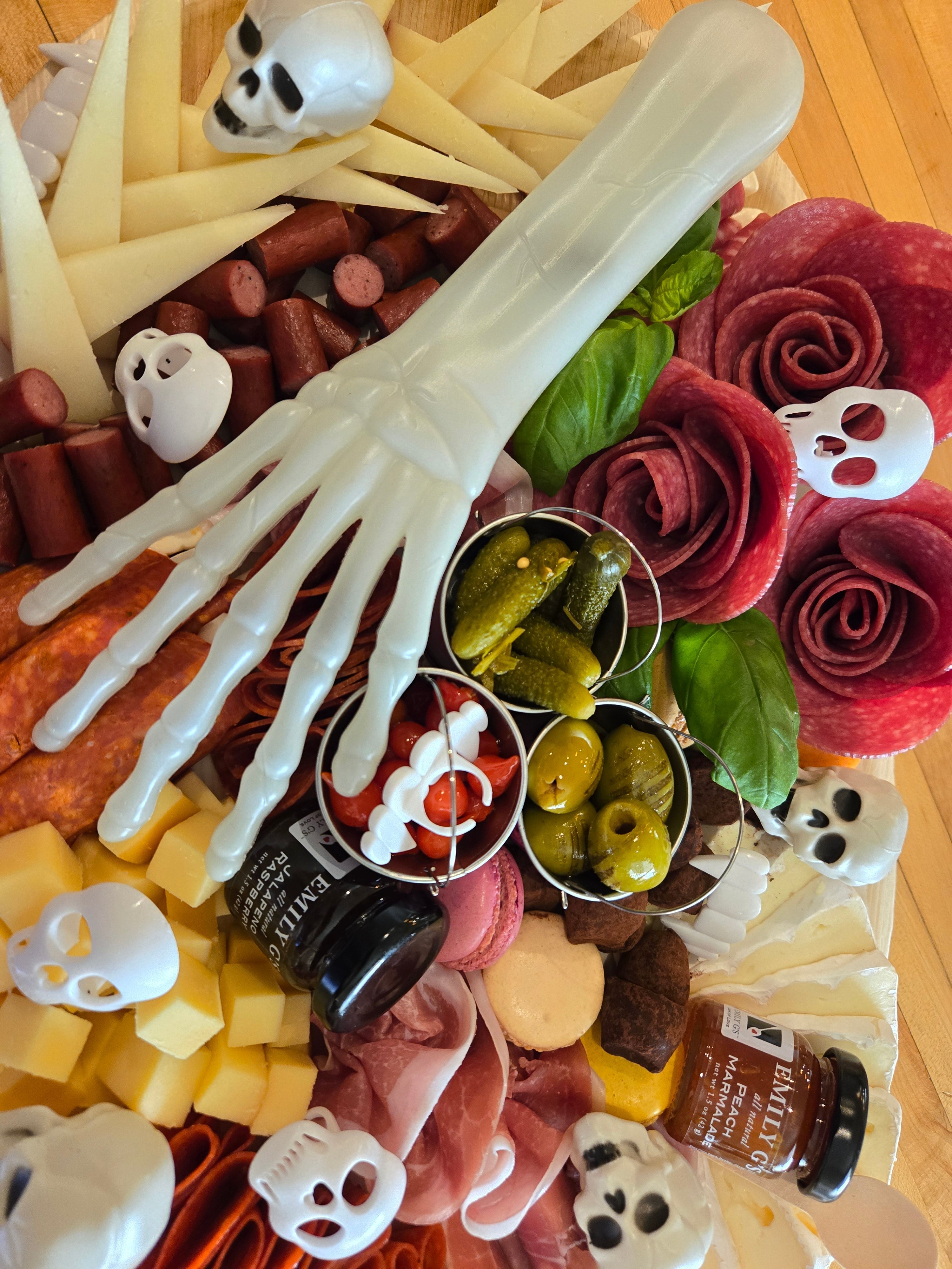 Spooky Halloween charcuterie board with a skeleton hand, salami roses, and skull decorations.