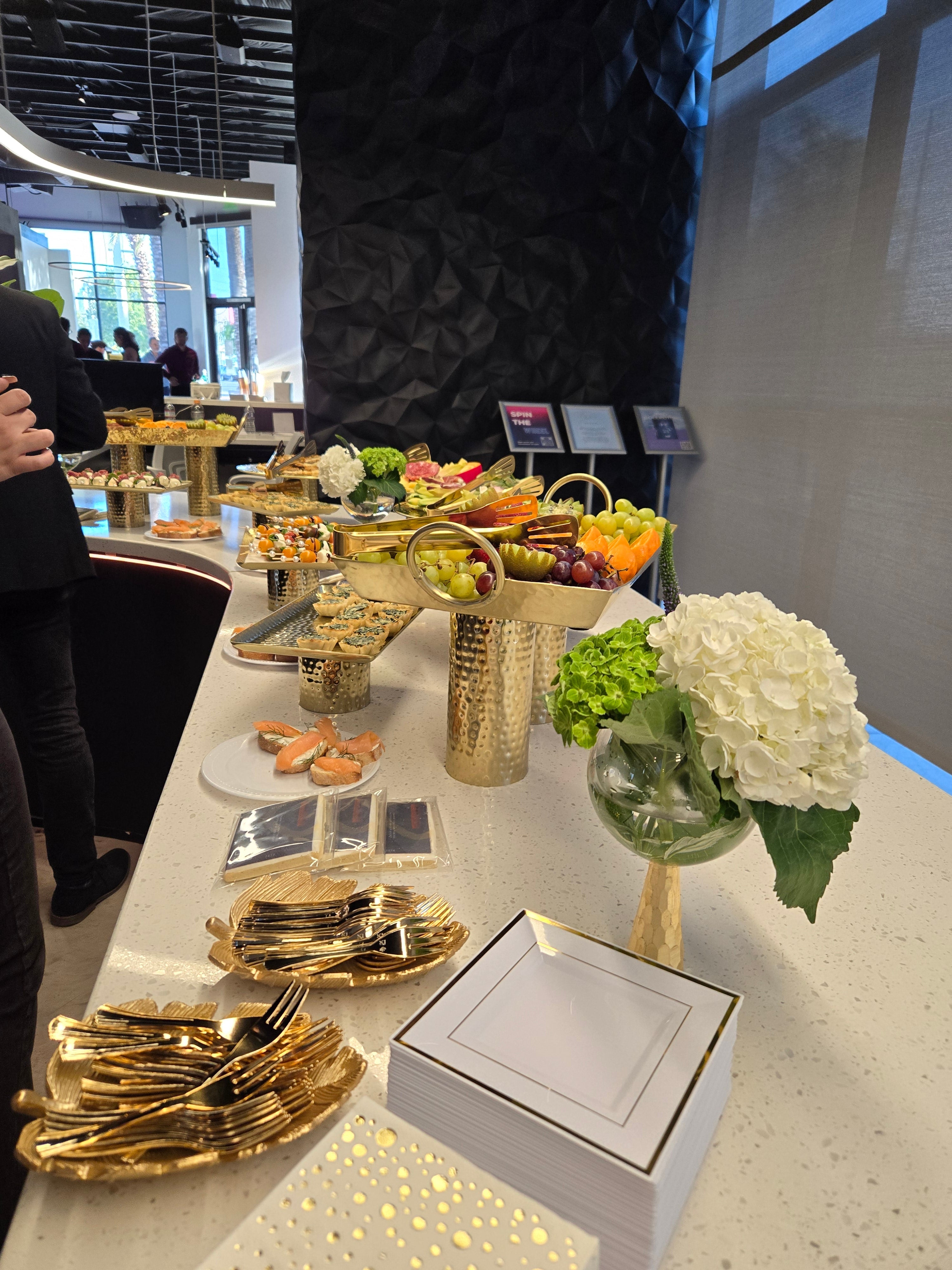 Elegant catering spread with fruit platters, appetizers, and gold cutlery for a corporate event.