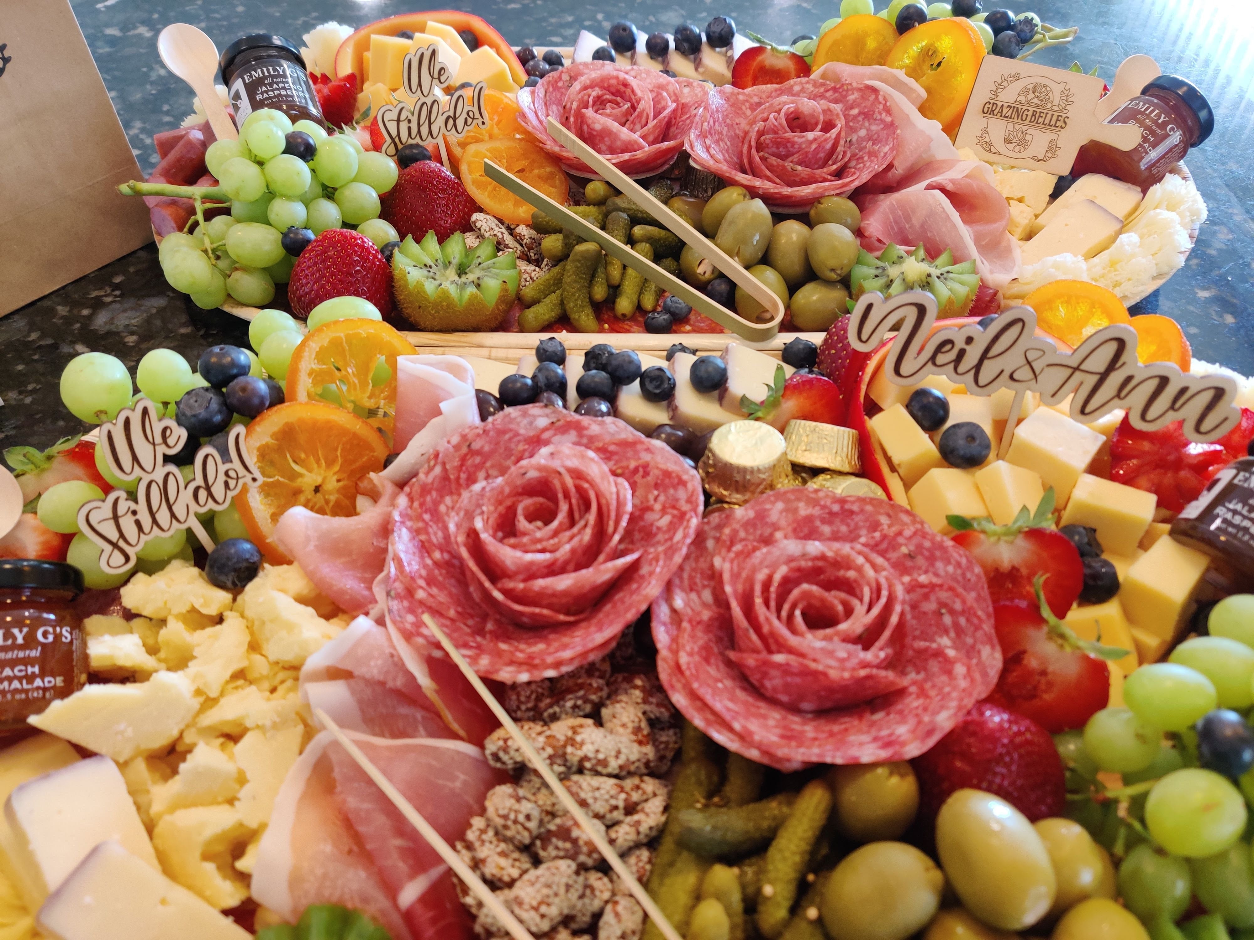Charcuterie grazing board with salami roses, assorted cheeses, fruits, and wedding decor.