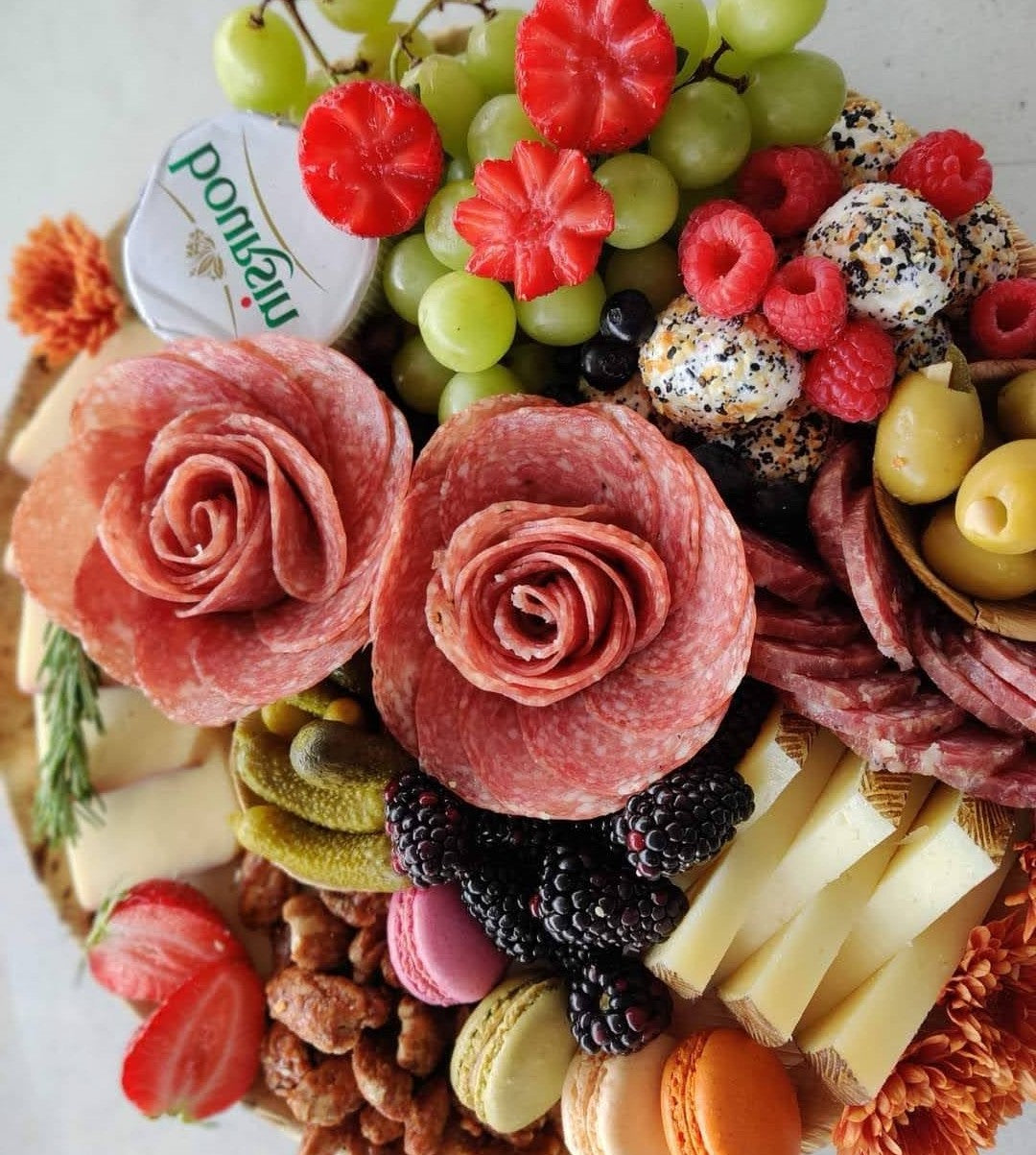 Charcuterie board with salami roses, grapes, berries, cheeses, and assorted grazing snacks.